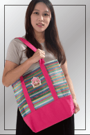 A woman carrying a pink and multicolour striped Spy x Family tote bag featuring an Anya Forger patch.