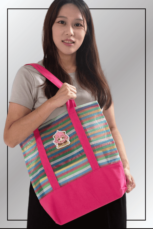 A woman carrying a pink and multicolour striped Spy x Family tote bag featuring an Anya Forger patch.